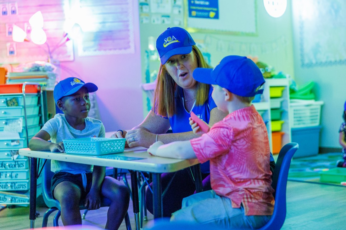 A Sunlight teacher sitting with two children during an open-house classroom activity.