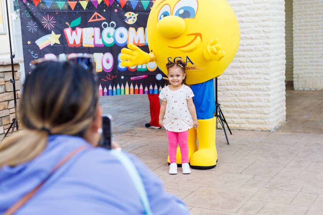 A young student smiling beside the Sunlight mascot on the first day of school.
