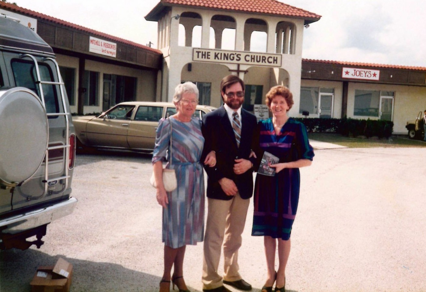 An archival photograph of three people outside a church meeting in a shopping plaza.